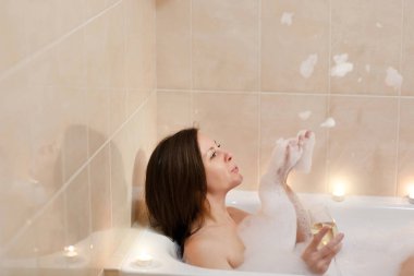 Uzun kahverengi saçlı ve düz çıplak vücut yalan, beyaz köpük küvet mum ışık banyoda, şarap cam kapalı içki alkol ile rahatlatıcı olan güzel seksi kadın.