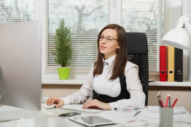 Takım elbise ve tablet ile masaya oturan gözlük güzel ciddi ve dalmış Kahverengi saç iş kadını ışık Office belgeleri ile modern monitör bilgisayarda çalışan bir kenara arıyorsunuz