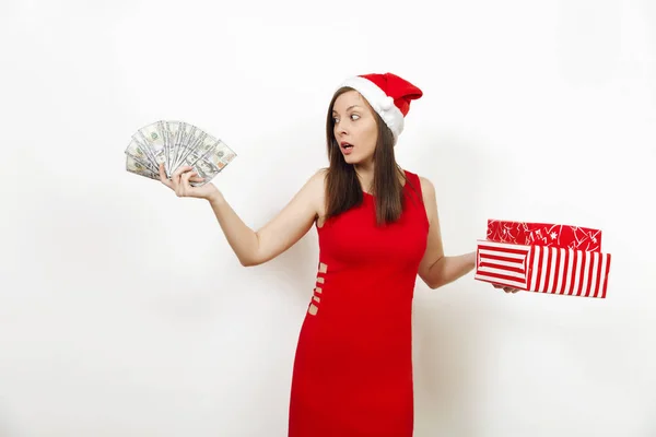 若い disconfused 赤いドレスと白い背景の上のギフト ボックスやお金紙幣を持ってクリスマス帽子で欲求不満な女です。プレゼント サンタ少女と分離された現金。新年休日 2018 コンセプト — ストック写真