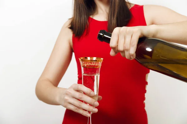 Belle femme heureuse caucasienne avec un sourire charmant en robe rouge versant du champagne de la bouteille dans le verre sur fond blanc. Santa girl isolé de près. Nouvel An 2018 et vacances de Noël — Photo
