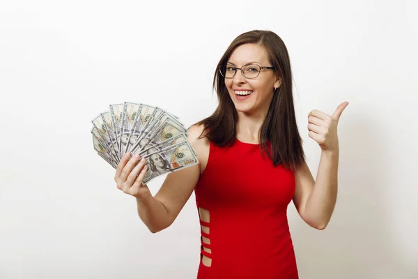 Jolie jeune femme d'affaires heureuse caucasienne avec un sourire charmant en robe rouge et des lunettes montrant pouce levé et tenant des billets d'argent sur fond blanc. Belle fille avec de l'argent isolé . — Photo