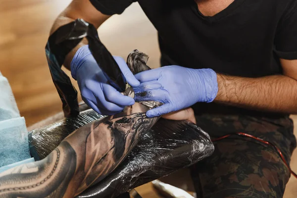 Profesyonel tattooer sanatçı tarafından makine siyah mürekkep bir kavanoz gelen adamın elini resim yapıyor kapatın. Vücudunda dövme sanatı. Dövme sanat yapmak için ekipman. Ana ışık studio dövmeli yapar.