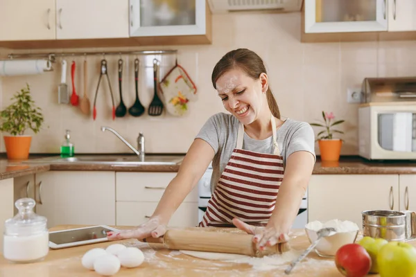Młody piękny szczęśliwy kobieta siedzi przy stole z mąki i tabletu, walcowania ciasta z wałkiem i będzie do przygotowania świąteczne ciasta w kuchni. Gotowanie w domu. Przygotowanie żywności. — Zdjęcie stockowe