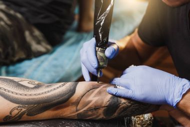 Profesyonel tattooer sanatçı tarafından makine siyah mürekkep bir kavanoz gelen adamın elini resim yapıyor kapatın. Vücudunda dövme sanatı. Dövme sanat yapmak için ekipman. Ana ışık studio dövmeli yapar.