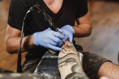 Profesyonel tattooer sanatçı tarafından makine siyah mürekkep bir kavanoz gelen adamın elini resim yapıyor kapatın. Vücudunda dövme sanatı. Dövme sanat yapmak için ekipman. Ana ışık studio dövmeli yapar.