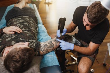 Profesyonel tattooer sanatçı tarafından makine siyah mürekkep bir kavanoz gelen adamın elini resim yapıyor. Vücudunda dövme sanatı. Dövme sanat yapmak için ekipman. Ana ışık studio dövmeli yapar.