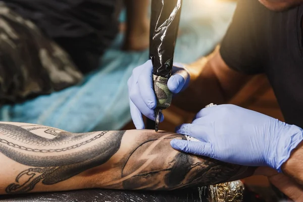 Profesyonel tattooer sanatçı tarafından makine siyah mürekkep bir kavanoz gelen adamın elini resim yapıyor kapatın. Vücudunda dövme sanatı. Dövme sanat yapmak için ekipman. Ana ışık studio dövmeli yapar.