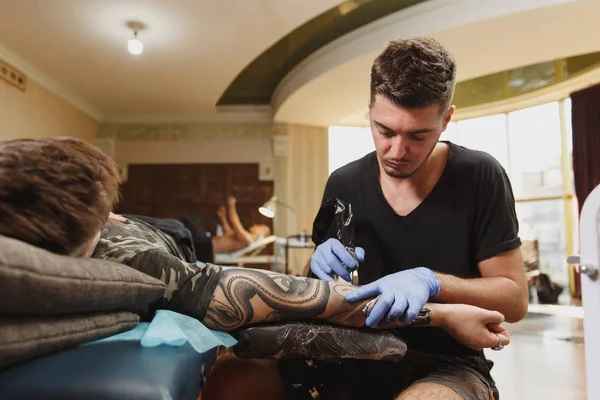 Профессиональный татуировщик рисует на руке человека черными чернилами из банки. Татуировка на теле. Оборудование для изготовления татуировок. Мастер делает татуировки в светлой студии . — стоковое фото
