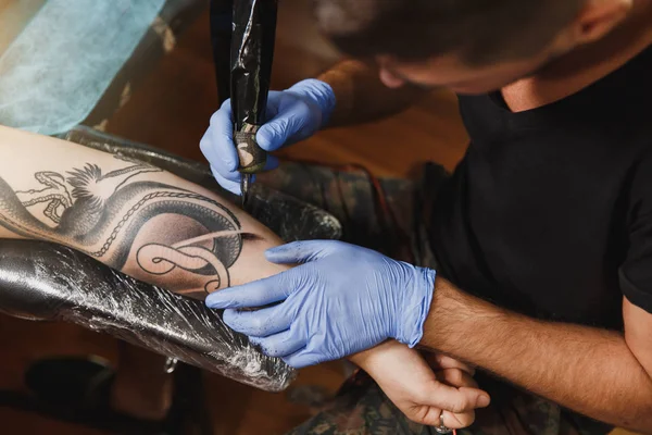 Profesyonel tattooer sanatçı tarafından makine siyah mürekkep bir kavanoz gelen adamın elini resim yapıyor kapatın. Vücudunda dövme sanatı. Dövme sanat yapmak için ekipman. Ana ışık studio dövmeli yapar.