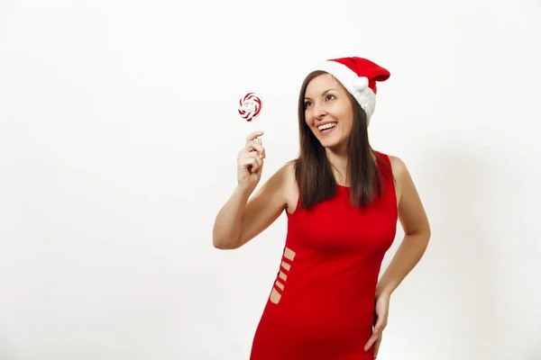 Vackra kaukasiska ung glad kvinna med frisk hud och charmiga leende i röd klänning och jul hatt hålla lollipop på vit bakgrund. Santa flicka isolerade. Nytt år holiday 2018 koncept — Stockfoto