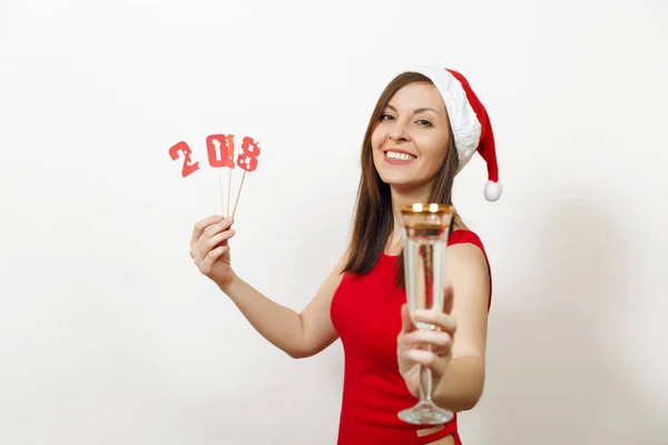 Hermosa mujer feliz joven caucásica con encantadora sonrisa en vestido rojo y sombrero de Navidad con número de tarjeta 2018 y copa de champán sobre fondo blanco. Santa chica aislada. Vacaciones de Año Nuevo — Foto de Stock