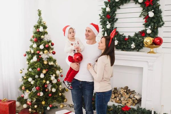 Şapkalı şirin küçük oğluyla mutlu anne. Büyük kırmızı Ağaç oyuncak topu ayakta dekore edilmiş yeni yıl ışık Oda evde Noel çelenk arka plan üzerinde çocuk çocuk. Aile, tatil 2018 kavramı.