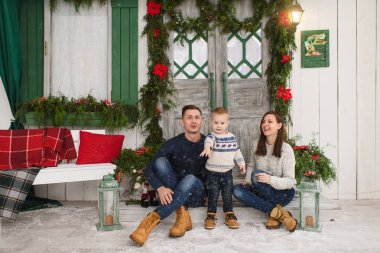 Mutlu anne ile küçük oğlu. Adımları ile hafif evinde kırmızı yeşil yeni yıl kapıdan evde dekore sundurma kar üzerinde oturan kazaklı oğlan çocuk. Noel keyfi. Aile ve tatil 2018 kavramı