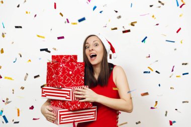 Çok şaşırmış mutlu kadın kırmızı elbise ve beyaz arka plan ve renkli konfeti hediye kutuları tutarak Noel şapka giymiş. Noel Baba hediye izole kızla. Yeni yıl tatil 2018 kavramı