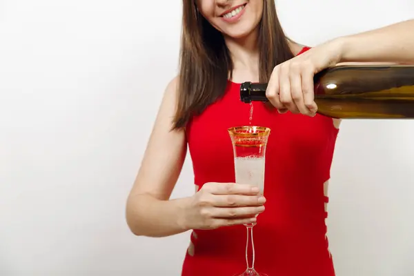 Belle femme heureuse caucasienne avec un sourire charmant en robe rouge versant du champagne de la bouteille dans le verre sur fond blanc. Santa girl isolé de près. Nouvel An 2018 et vacances de Noël — Photo