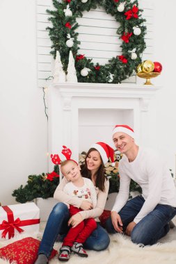 Kırmızı şapkalı şirin küçük oğluyla mutlu anne. Çocuk çocuk dekore edilmiş yeni yıl ağacı ve hediye kutuları arka planda Noel çelenk ışık odada evde oturuyor. Aile, tatil 2018 kavramı.