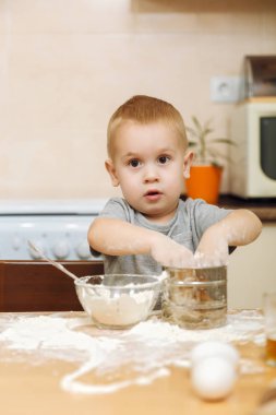 Küçük çocuk çocuk anne Noel ışık mutfakta zencefilli bisküvi pişirmek için yardımcı olur. Gri T-shirt hafta sonu sabah evde masada demir elek ve un ile 2-3 yıl içinde mutlu sarışın çocuk.