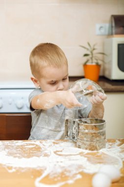 Küçük çocuk çocuk anne Noel ışık mutfakta zencefilli bisküvi pişirmek için yardımcı olur. Gri T-shirt hafta sonu sabah evde masada demir elek ve un ile 2-3 yıl içinde mutlu sarışın çocuk.