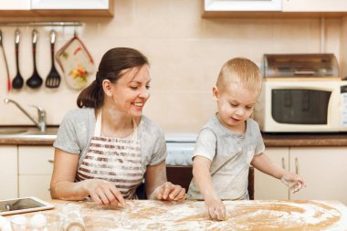 Küçük çocuk çocuk anne Noel masanın üzerine tablet ile ışık mutfakta zencefilli bisküvi pişirmek için yardımcı olur. Mutlu aile anne 30-35 yıl ve çocuk 2-3 hafta sonu sabah evde. İlişki kavramı