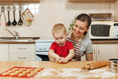Küçük çocuk çocuk anne Noel ışık mutfakta zencefilli bisküvi pişirmek için yardımcı olur. Mutlu aile anne 30-35 yıl ve 2-3 rulo dışarı hamur ve çerezler de uygunbir çocuk ev. İlişki ve sevgi kavramı