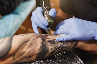 Profesyonel tattooer sanatçı tarafından makine siyah mürekkep bir kavanoz gelen adamın elini resim yapıyor kapatın. Vücudunda dövme sanatı. Dövme sanat yapmak için ekipman. Ana ışık studio dövmeli yapar.