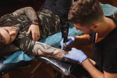 Profesyonel tattooer sanatçı tarafından makine siyah mürekkep bir kavanoz gelen adamın elini resim yapıyor. Vücudunda dövme sanatı. Dövme sanat yapmak için ekipman. Ana ışık studio dövmeli yapar.