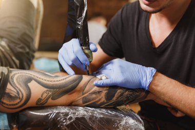 Profesyonel tattooer sanatçı tarafından makine siyah mürekkep bir kavanoz gelen adamın elini resim yapıyor kapatın. Vücudunda dövme sanatı. Dövme sanat yapmak için ekipman. Ana ışık studio dövmeli yapar.