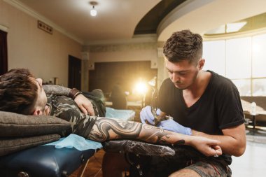 Profesyonel tattooer sanatçı tarafından makine siyah mürekkep bir kavanoz gelen adamın elini resim yapıyor. Vücudunda dövme sanatı. Dövme sanat yapmak için ekipman. Ana ışık studio dövmeli yapar.