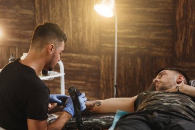 Profesyonel tattooer sanatçı tarafından makine siyah mürekkep bir kavanoz gelen adamın elini resim yapıyor. Vücudunda dövme sanatı. Dövme sanat yapmak için ekipman. Ana ışık studio dövmeli yapar.