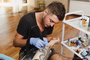 Profesyonel tattooer sanatçı tarafından makine siyah mürekkep bir kavanoz gelen adamın elini resim yapıyor. Vücudunda dövme sanatı. Dövme sanat yapmak için ekipman. Ana ışık studio dövmeli yapar.
