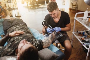 Profesyonel tattooer sanatçı tarafından makine siyah mürekkep bir kavanoz gelen adamın elini resim yapıyor. Vücudunda dövme sanatı. Dövme sanat yapmak için ekipman. Ana ışık studio dövmeli yapar.