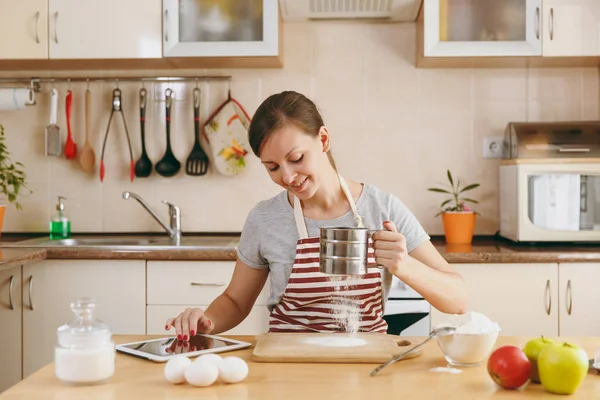 Genç, güzel ve mutlu bir kadın un elek ve seyir için Noel kek tablet mutfak için bir reçete ile sifts. Pişirme ev. Yemek hazırlamak.
