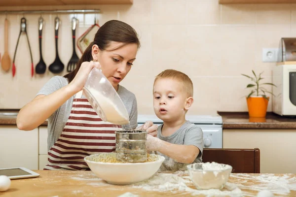 Jongen-jongetje helpt moeder om te koken kerst gember koekje in lichte keuken met tablet op tafel. Gelukkige familie moeder 30-35 jaar en kind 2-3 in weekend's ochtends thuis. Begrip van de relatie — Stockfoto