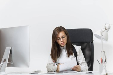 Takım elbise ve masa başında oturan gözlük güzel ciddi ve dalmış Kahverengi saç iş kadını bilgisayar başında beyaz zemin üzerine ışık Office belgeleri ile modern İzleyicisi ile çalışma