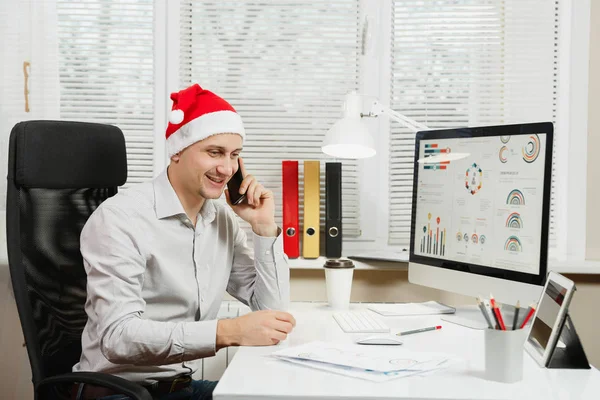 Hombre de negocios guapo en camisa y sombrero rojo de Navidad sentado en — Foto de Stock