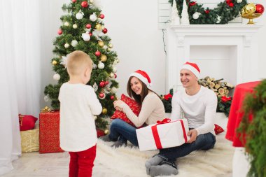 Mutlu neşeli anne ile şirin küçük oğlu kırmızı şapkalı. Çocuk çocuk odasında ışık evde yılbaşı ağacı ve hediye kutuları ile dekore edilmiştir. Noel keyfi. Aile, sevgi ve tatil 2018 kavramı.