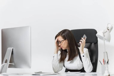 Güzel yorgun ve beyaz arka plan üzerinde sorunlarını çözme cep telefonda konuşurken ışık Office belgeleri ile modern bilgisayarda çalışan iş kadını masada oturan takım elbiseli stres