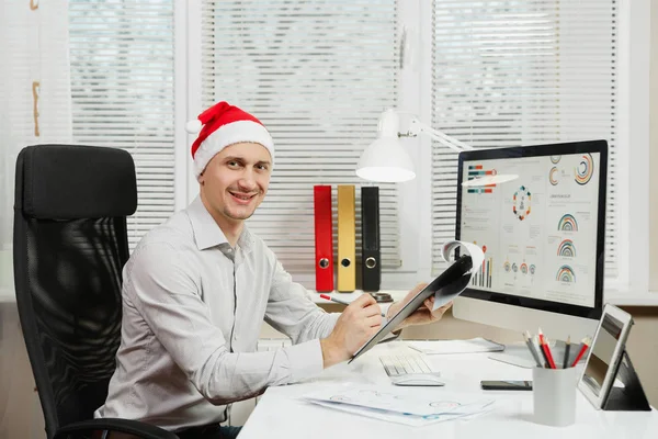 Guapo sonriente hombre de negocios en camisa y sombrero rojo de Navidad sentarse — Foto de Stock