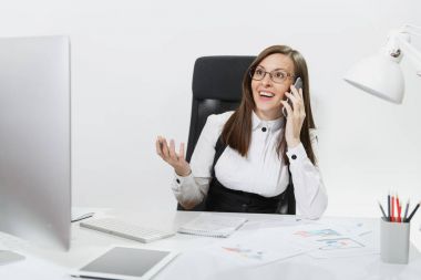Masa başında oturan takım elbiseli ışık belgede ile çağdaş bilgisayarda çalışan, cep telefonu üzerinde konuşurken, beyaz arka plan üzerinde hoş sohbet iletken oldukça gülümseyen iş kadını