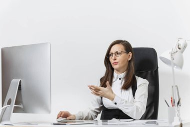 Takım elbise ve masa başında oturan gözlük güzel sürpriz ve kızgın Kahverengi saç iş kadını bilgisayar başında beyaz zemin üzerine ışık Office belgeleri ile modern İzleyicisi ile çalışma