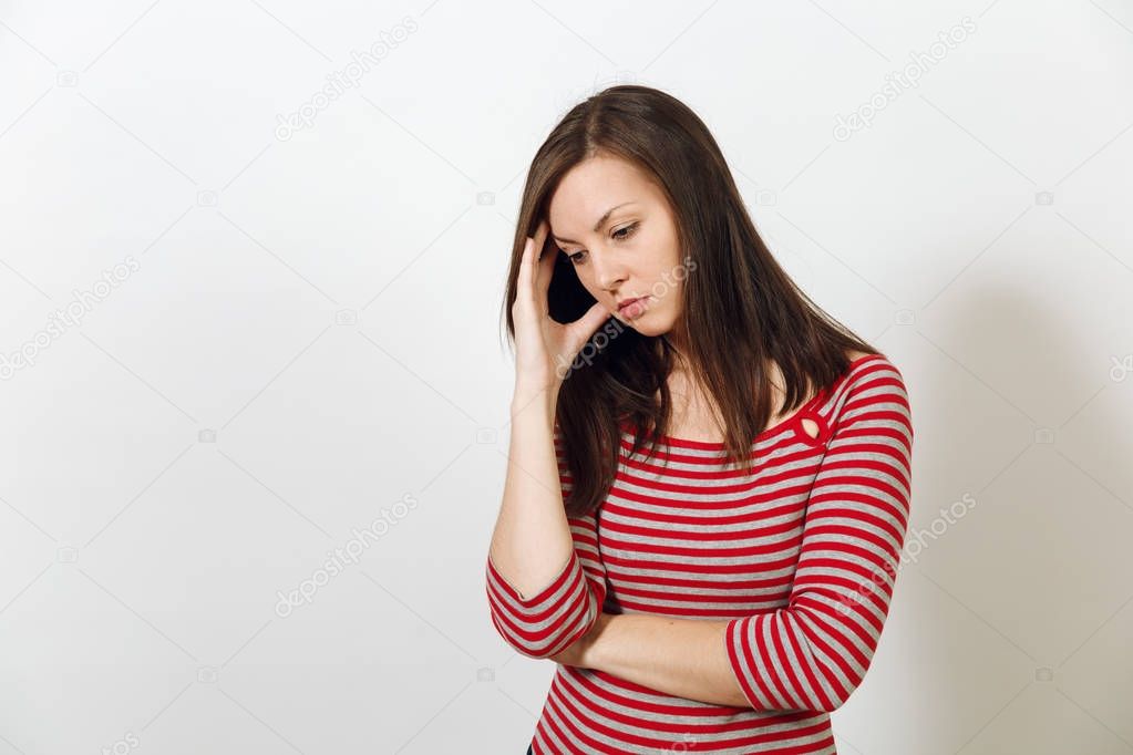 Pretty European young worried and pensive brown-haired woman with healthy clean skin, dressed in casual red and grey clothes lost in thought and conjectures, on a white background. Emotions concept.