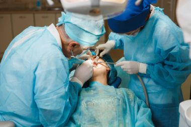 Üniforma ve kadın asistanı erkek eski profesyonel diş hekimi cerrahı Kliniği hafif ofis modern araçlar ekipman ile işlem yükleme diş implant diş kadın hastanın gerçekleştirmek için yardımcı olur.