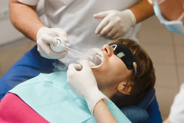 Närbild av processen att förbereda och installera keramiska tandkrona. Manliga professionella tandläkare hjälper till att behandla tänderna av kvinnlig patient på klinik ljus kontor med moderna verktyg utrustning. Öppen mun. — Stockfoto