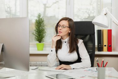 Takım elbise ve tablet ile masaya oturan gözlük güzel ciddi ve dalmış Kahverengi saç iş kadını ışık Office belgeleri ile modern monitör bilgisayarda çalışan bir kenara arıyorsunuz