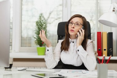 Işık Office belgeleri ile çağdaş bilgisayarda çalışan güzel ciddi iş kadın takım elbise ve masa başında oturan gözlük cep telefonu üzerinde sorunları çözme bir kenara seyir konuşurken