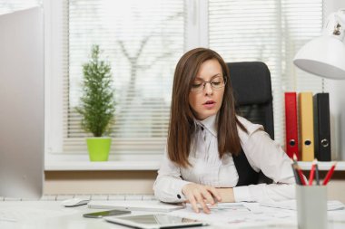 Takım elbise ve tablet ile masaya oturan gözlük güzel ciddi ve dalmış Kahverengi saç iş kadını ışık Office belgeleri ile modern monitör bilgisayarda çalışan bir kenara arıyorsunuz