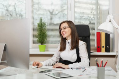 Bir kenara ışık Office belgeleri ile modern İzleyicisi ile bilgisayarda çalışan güzel gülümseyen brown-iş kadın takım elbise ve tablet ile masaya oturan gözlük arıyorum