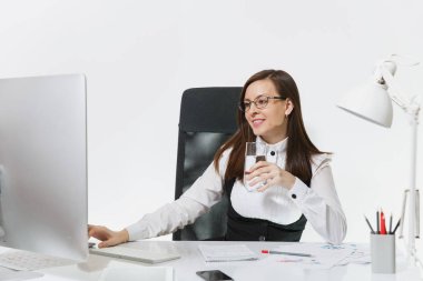 Beyaz arka plan üzerinde ışık Office belgeleri ile modern İzleyicisi ile bilgisayarda çalışan güzel gülümseyen brown-iş kadın takım elbise ve gözlük ile saf su, cam masa başında oturan