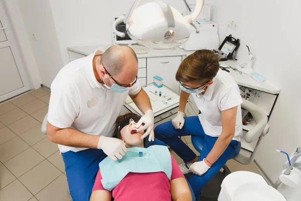 Proceso de preparación e instalación de corona de cerámica dental. El dentista profesional masculino y el asistente femenino ayudan a tratar los dientes de la paciente en la oficina ligera clínica con equipos de herramientas modernos . — Foto de Stock