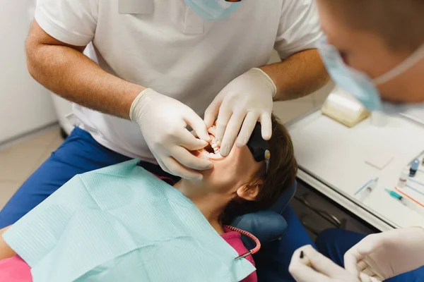 Närbild av processen att förbereda och installera keramiska tandkrona. Manliga professionella tandläkare hjälper till att behandla tänderna av kvinnlig patient på klinik ljus kontor med moderna verktyg utrustning. Öppen mun. — Stockfoto